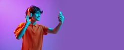 Video call. Young man talking on phone isolated over pink-purple background in neon light. Future, gadgets, digital technology concept. Human emotion, facial expressions. Copy space for ad, design.