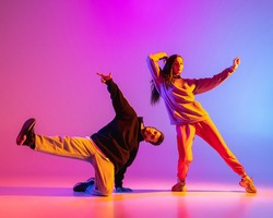 Brakedancing. Two young people, guy and girl, dancing contemporary dance over pink background in neon light. Modern dance aesthetics concept