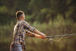 Sunset fishing. Cropped portrait of young man spending time outdoors in countryside near river casting fishing rod. Active weekend. Resting on warm summer day. Concept of leisure time activity, ad