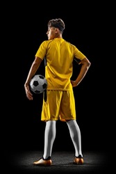 Back view full-length portrait of young handsome football player in yellow uniform isolated over black background. Concept of action, team sport game, energy, vitality. Copy space for ad.