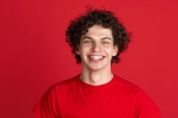 Happiness. Portrait of young cheerful man in casual cloth smiling isolated over red background. Concept of feelings, youth, fashion, facial expression, emotions, lifestyle, ad