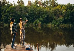 Nice day out. Unusual romantic date in countryside. Young beautiful couple standing on pier and fishing. Beauty of nature. Summer weekends. Fresh air breathing. Concept of leisure time activity, ad