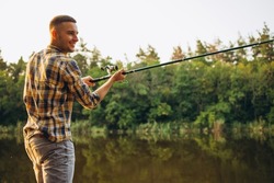 Sunset fishing. Cropped portrait of young man spending time outdoors in countryside near river and fishing. Active weekend. Resting on warm summer day. Concept of leisure time activity, ad