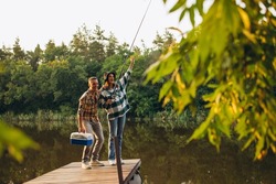 Wow, fish. Unusual romantic date in countryside. Young beautiful couple standing on pier and fishing. Beauty of nature. Summer weekends. Fresh air breathing. Concept of leisure time activity, ad
