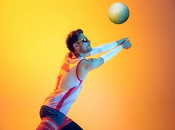 Portrait of young man, beach volleyball player in motion, training, playing isolated on yellow studio background in neon light. Concept of sport, action, team game, active lifestyle, health, hobby, ad