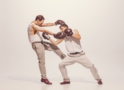 Portrait of two men playing, boxing in gloves isolated over grey studio background. Artistic friends. Concept of sport, hobby, work, active lifestyle, retro fashion. Copy space for ad