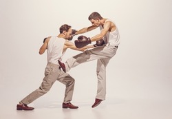 Portrait of two men playing, boxing in gloves isolated over grey studio background. Dynamic image of fight. Concept of sport, hobby, work, active lifestyle, retro fashion. Copy space for ad
