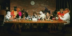 Group of people standing, sitting at the long table in different costumes, indoors and lively communicating. Funny, modern replica of last supper painting. Comical life situation
