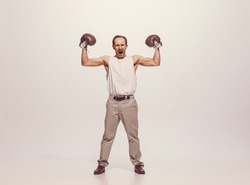 Portrait of muscular man in vintage clothes showing muscles in boxing gloves, posing isolated over grey studio background. Concept of sport, hobby, active lifestyle, retro fashion. Copy space for ad