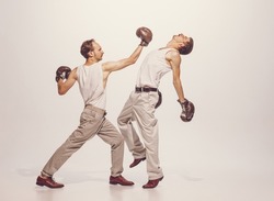 Portrait of two men playing, boxing in gloves isolated over grey studio background. Straight punch. Concept of sport, hobby, work, active lifestyle, retro fashion. Copy space for ad