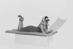Summer vacation. Monochrome portrait of young beautiful woman lying on inflatable mattress and reading magazine. Retro vintage style, 70s, 80s fashion. Copy space for ad