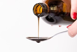 Bottle pouring a liquid on a spoon. Isolated on a white background. Pharmacy and healthy background.Cough and cold drug. Woman´s hand holding a bottle.