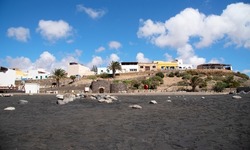 Panoramic view taken from the black sandy beach of the village of Ajuy with small simple coloured houses typical of Fuerteventura and surrounded by a desert and volcanic landscape in Canary Islands