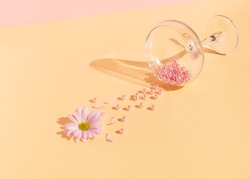 Creative composition with pink pearls and flower spilling out of champagne glass on bright peach puff background. Minimal spring love concept.