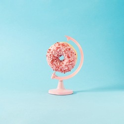 Creative composition with pink globe stand and colorful cream donut against pastel blue background.