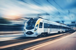 High speed passenger train in motion on the railway station at sunset in Europe. Modern intercity train on railway platform with motion blur effect. Urban scene with railroad. Railway transportation