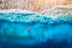 Aerial view of woman swimming on the pink swim ring in the transparent sea in Oludeniz. Summer seascape with girl, beach, beautiful waves, blue water at sunset. Top view. Travel and holiday. Resort