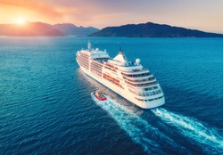 Cruise ship at harbor. Aerial view of beautiful large white ship at sunset. Colorful landscape with boats in marina bay, sea, colorful sky. Top view from drone of yacht. Luxury cruise. Floating liner