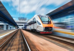 High speed train in motion on the railway station at sunset. Modern intercity passenger train with motion blur effect on the railway platform. Industrial. Railroad in Europe. Commercial transportation