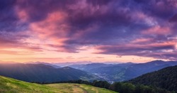 Mountains at beautiful sunset in summer. Colorful panoramic landscape with meadows with green grass, sky with vibrant clouds, mountains with forest. Trail on the hill. Travel and nature. Scenery