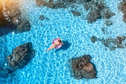 Aerial view of a young woman swimming with pink swim ring in blue sea at sunset in summer. Tropical landscape with girl, stones and rocks in clear water, sandy beach. Top view. Lefkada island, Greece