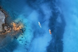 Aerial view of people on floating kayaks on blue sea, rocky coast, trees at sunrise in summer. Blue lagoon, Oludeniz, Turkey. Tropical landscape. Sup boards on clear water. Top view of canoe. Tourism