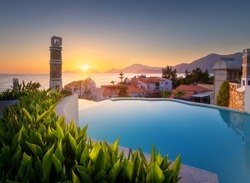 Beautiful swimming pool, green bush and orange roofs at colorful sunset. Blue water, sea coast, architecture, flowers in summer. Luxury resort. Oludeniz, Turkey. Amazing landscape with pool, houses