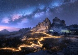 Milky Way, car light trails on mountain road, high rocks at starry night in summer. Tre cime, Dolomites, Italy. Colorful landscape with blurred light trails, hills, mountain peaks, sky with stars