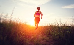 Young woman running on a rural road at sunset in summer field. Lifestyle sports background  