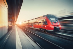 Beautiful railway station with modern high speed red commuter train with motion blur effect at colorful sunset in Nuremberg, Germany. Railroad with vintage toning
