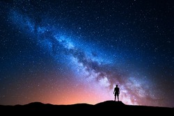 Milky Way. Beautiful night sky with stars and silhouette of a standing alone man on the mountain. Blue milky way and man on the hill. Background with galaxy and silhouette of a man. Universe