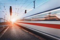 Modern high speed passenger train on railroad in motion at sunset. Blurred commuter train. Railway station at dusk with vintage toning. Travel background, railway tourism. Industrial landscape. Train