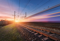 High speed passenger train in motion on railroad at sunset. Blurred commuter train. Railway station against sunny sky. Railroad travel, railway tourism. Rural industrial landscape. Concept