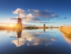 Windmills at sunrise. Rustic landscape with amazing dutch windmills near the water canals with blue sky and clouds reflected in water. Beautiful morning in Kinderdijk, Netherlands in spring. Travel