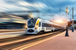 High speed train in motion at the railway station at sunset. Modern european intercity train on the railway platform with motion blur effect. Industrial scene with moving passenger train on railroad