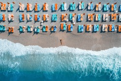 Beautiful young woman on the sea at sunrise in Oludeniz, Turkey. Aerial view of lying woman on the beach with colorful chaise-lounges. Top view from drone. Seascape with girl, azure water and waves