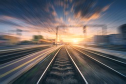 Railway station with motion blur effect. Blurred railroad. Industrial conceptual landscape with blurred railway station, buildings, blue sky with colorful clouds and sun. Railway track. Background