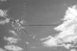 A hole in the glass from a piece of ammunition. window glass pierced by a bullet. broken glass. blue sky on the background. Horizontal image. black and white image