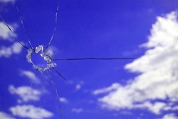 A hole in the glass from a piece of ammunition. window glass pierced by a bullet. broken glass. blue sky on the background. Horizontal image.