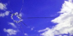 A hole in the glass from a piece of ammunition. window glass pierced by a bullet. broken glass. blue sky on the background. Horizontal image. Banner for insertion into site.