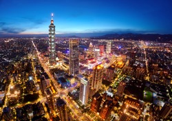 Aerial panorama of Downtown Taipei at dusk, the vibrant capital of Taiwan, with 101 Tower standing out among skyscrapers in Xinyi Commercial District and city lights dazzling under blue twilight sky