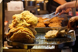 A stall vendor frying in boiling oil the crispy deep-fried chicken cutlets, one of local people's favorite street-foods, in Shilin Night Market, Taipei, where many traditional snacks can be savored