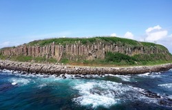 Beautiful coastal basalt columns of Tongpan Island under blue sunny sky, with a hiking path running under the cliffs and furious waves beating the off shore rocks, in Magong, Penghu County, Taiwan