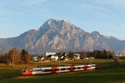 Scenery of a train dashing in the field on a beautiful autumn day and rugged Traunstein Mountain towering in the background by Lake Traunsee under blue sunny sky, in Altmünster, Salzkammergut, Austria