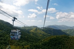 A panoramic view from a gondola of Ngong Ping 360 cable car, overlooking green lush forests on the mountainside and the giant Tian Tan Buddha Statue on a mountaintop in Lantau Island, Hong Kong, China