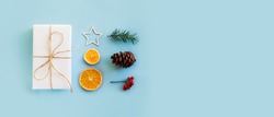 Christmas composition with eco crafted gift, dried orange, cone, xmas tree, gift and wood star. Natural minimal new year concept, top view, isolated, flat lay, copy space on blue background, banner