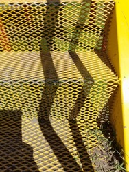 Yellow steel stairway for children's playground with shadow lines forms a curious abstract design with a textured background of the steps
