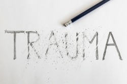 Erasing trauma. Trauma written on white paper with a pencil, partially erased with an eraser. Symbolic for overcoming trauma or treating trauma.  