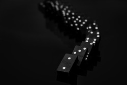 Black vintage falling dominoes on a black background, selective focus. WB photo.