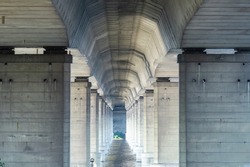 Tunnel from column under road bridge in city. Row pillars and group arches. Built structure prefabricated concrete of overpass. Details architecture of bridge on river. Technology construction.